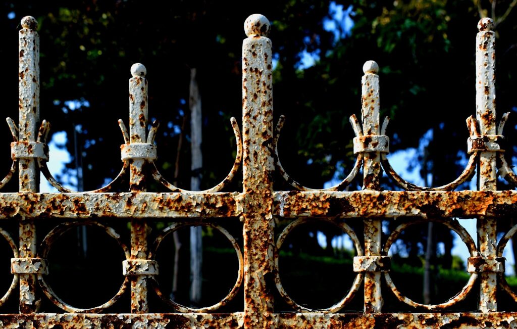Photo of the top of a decorative iron fence, with trees in the background.
