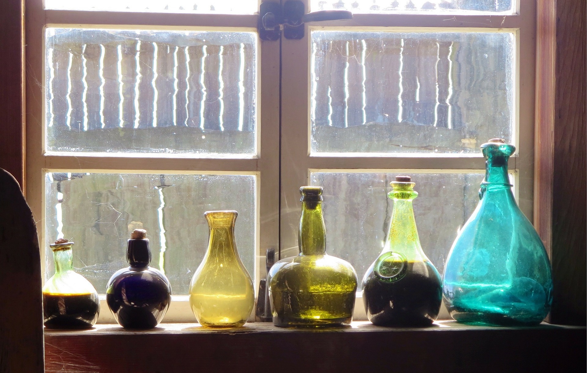 Photo of old bottles on a windowsill, catching the light from outside.