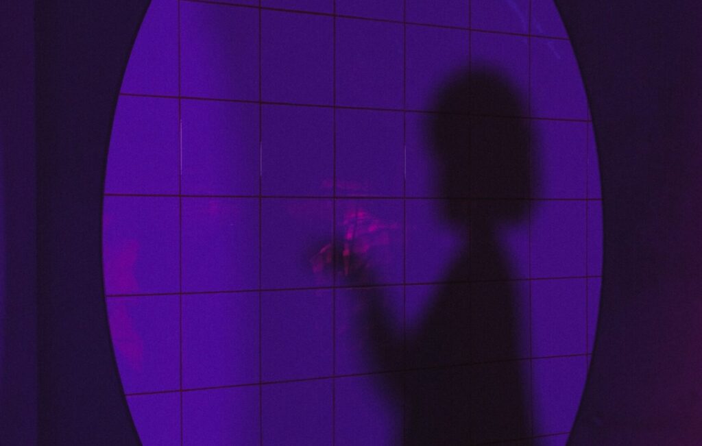Silhouette of a person on a tiled wall. The light is purple and round, like a spotlight.