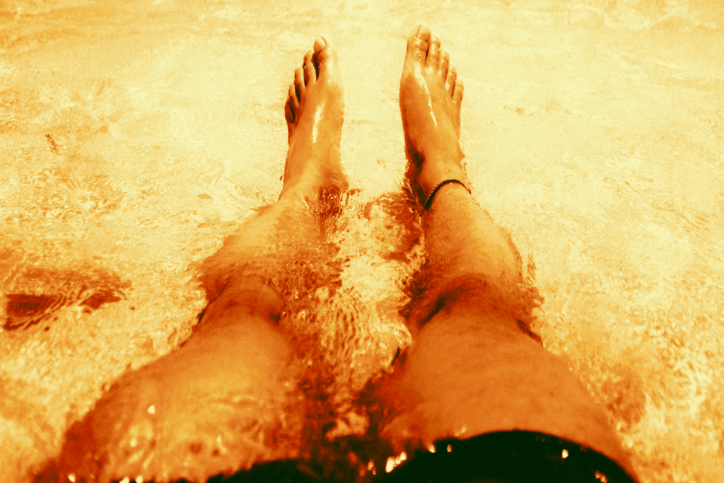 Photo of a person's legs stretched out in front of them as they are bathing in the sea. There is a distinct orange hue to the image.