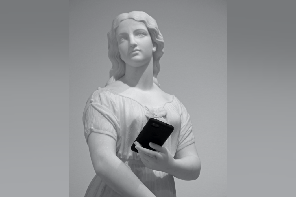 Greyscale image of an unpainted white statue of a woman holding a black mobile phone in one hand as she stares into the distance.